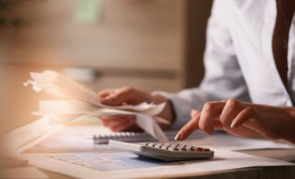 Close up of accountant holding bills and working on calculator in the office.